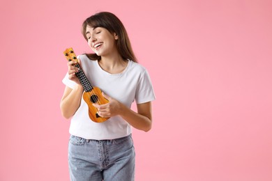 Photo of Happy woman playing ukulele on pink background