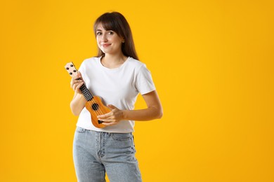 Young woman playing ukulele on orange background, space for text