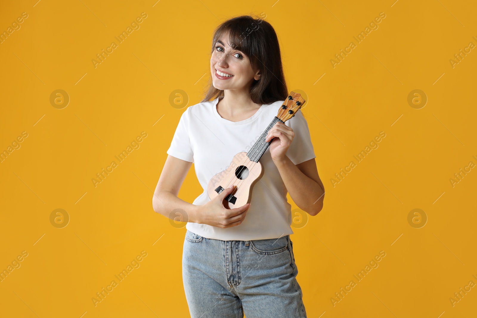 Photo of Happy woman playing ukulele on orange background