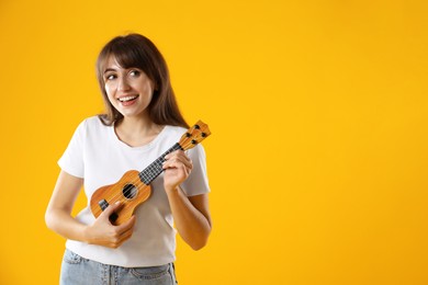 Photo of Happy woman playing ukulele on orange background, space for text