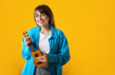 Photo of Happy woman playing ukulele on orange background, space for text