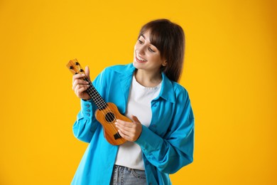 Happy woman playing ukulele on orange background