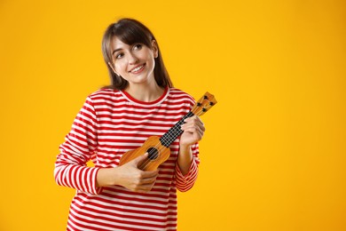 Photo of Happy woman playing ukulele on orange background, space for text