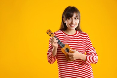 Happy woman playing ukulele on orange background, space for text