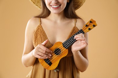 Photo of Woman playing ukulele on beige background, closeup