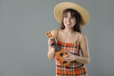 Photo of Happy woman playing ukulele on grey background, space for text