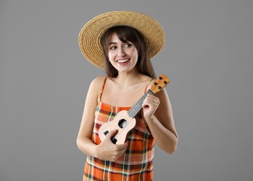 Happy woman playing ukulele on grey background