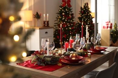 Photo of Christmas table setting with stylish dishware, glasses and burning candles in festive decorated room