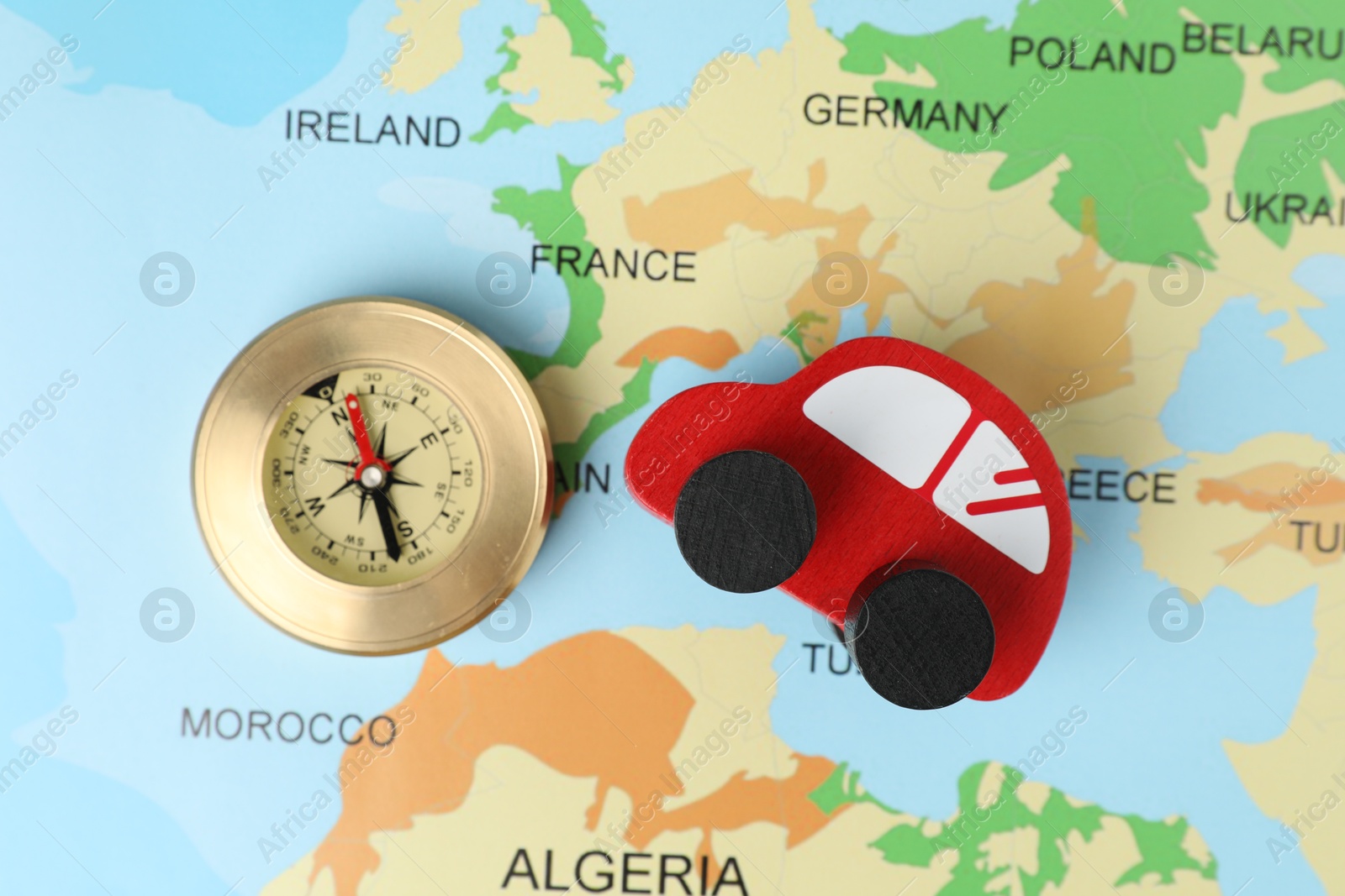 Photo of Red wooden toy car and compass on world map, top view. Road trip