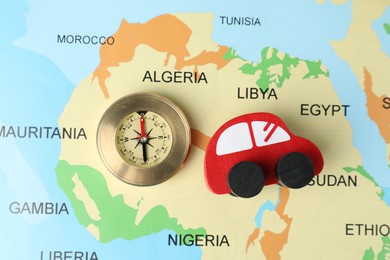 Photo of Red wooden toy car and compass on world map, top view. Road trip