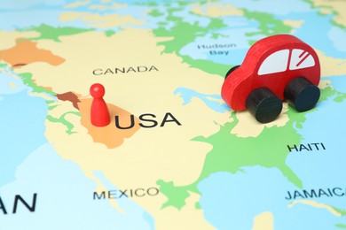 Photo of Red wooden toy car and human figure on world map. Road trip