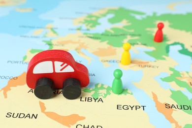 Photo of Red wooden toy car and human figures on world map. Road trip planning