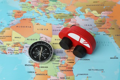 Photo of Red wooden toy car and compass on world map. Road trip