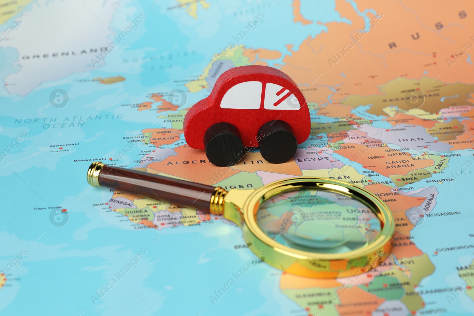 Photo of Red wooden toy car and magnifying glass on world map. Road trip