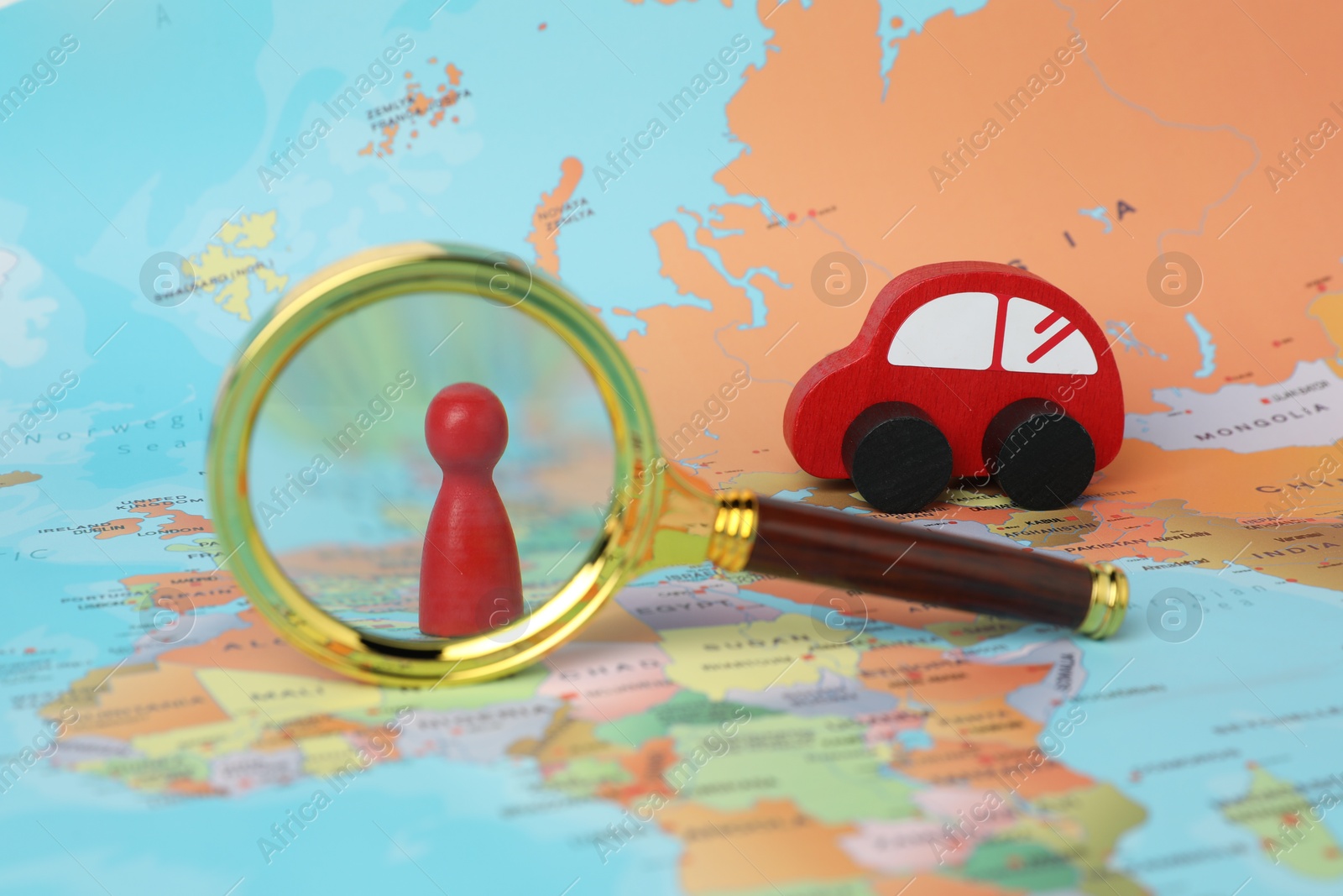 Photo of Red wooden toy car, magnifying glass and human figure on world map. Road trip