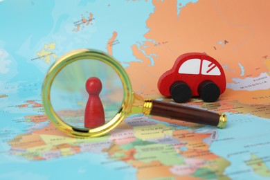 Photo of Red wooden toy car, magnifying glass and human figure on world map. Road trip