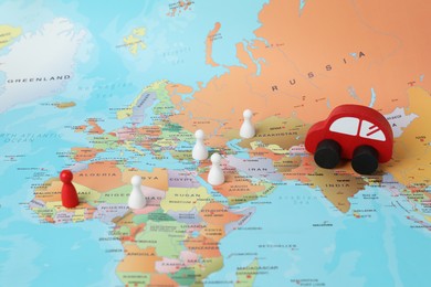 Photo of Red wooden toy car and human figures on world map. Road trip planning