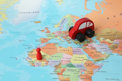 Photo of Red wooden toy car and human figure on world map. Road trip