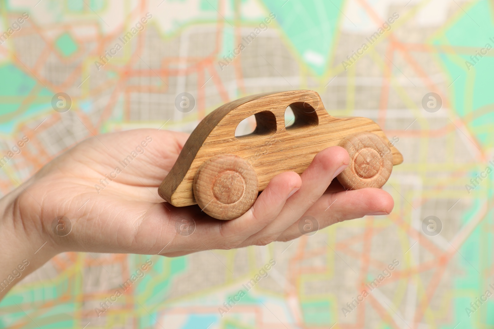 Photo of Woman with toy wooden car against city map, closeup. Road trip