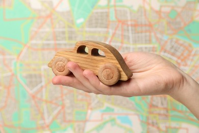 Photo of Woman with toy wooden car against city map, closeup. Road trip