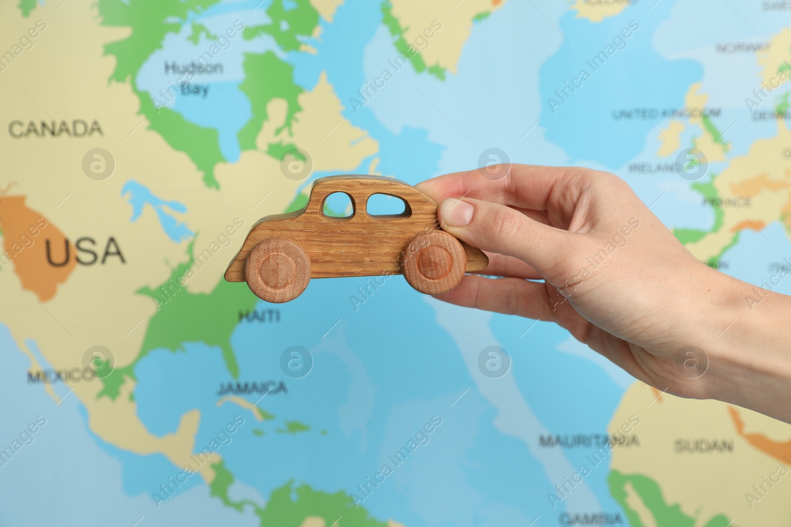 Photo of Woman with toy wooden car against world map, closeup. Road trip