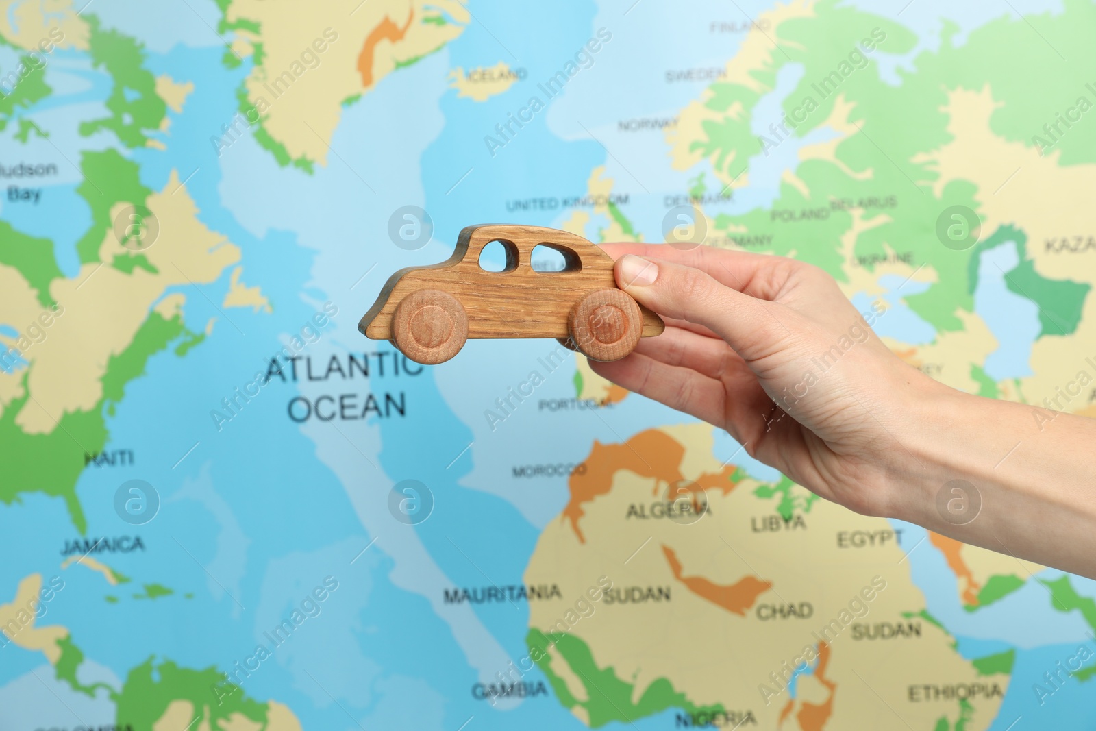 Photo of Woman with toy wooden car against world map, closeup. Road trip