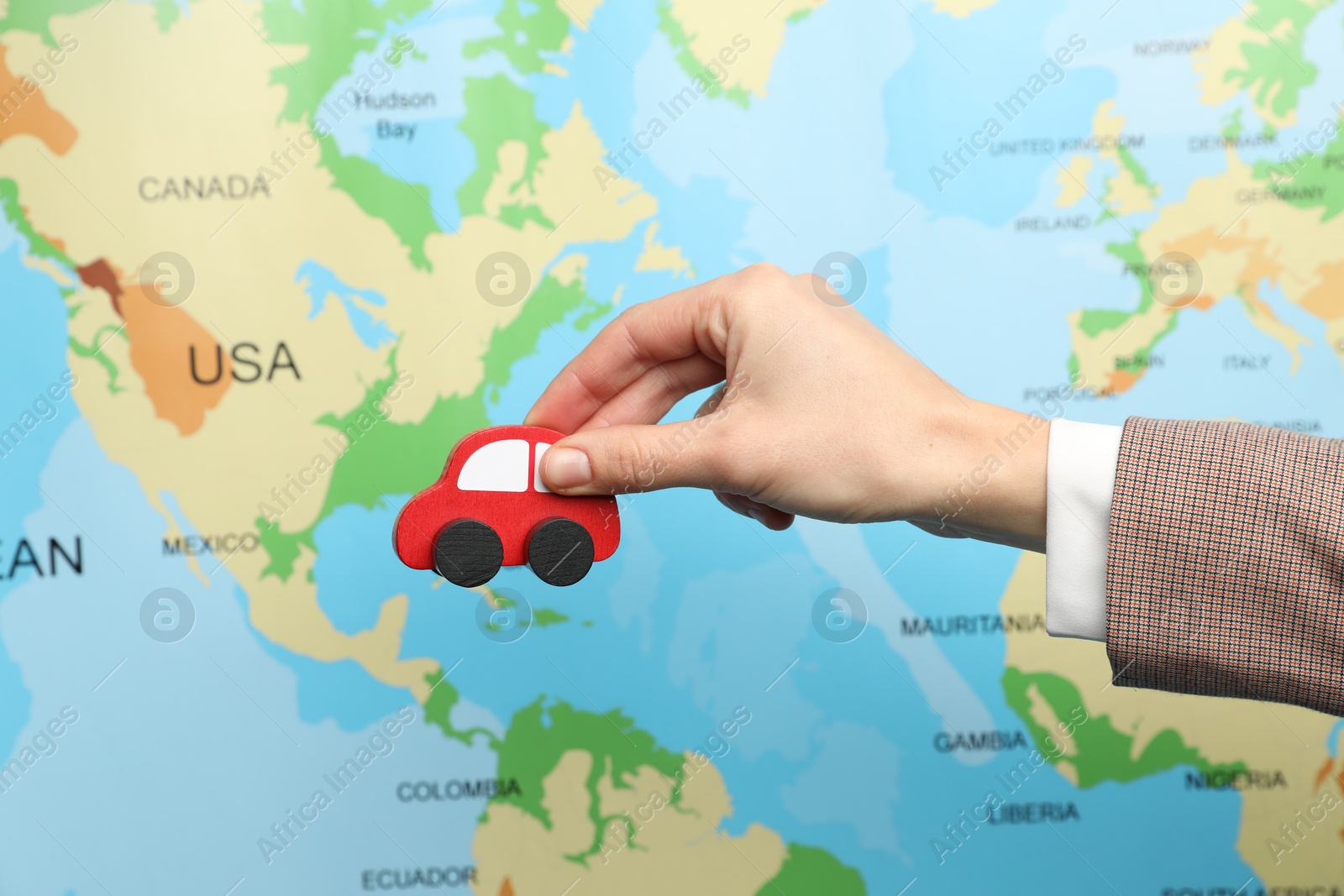 Photo of Woman with red toy car against world map, closeup. Road trip