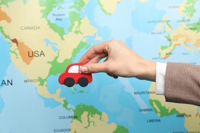 Photo of Woman with red toy car against world map, closeup. Road trip