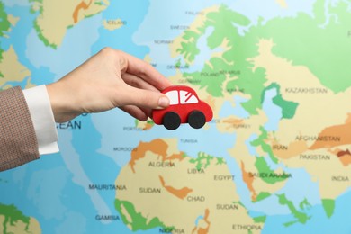 Photo of Woman with red toy car against world map, closeup. Road trip