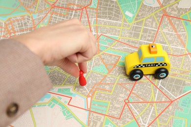 Photo of Woman putting red human figure on city map near toy taxi car, closeup. Road trip