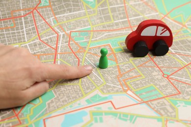 Photo of Woman pointing at city map near human figure and toy car, closeup. Road trip