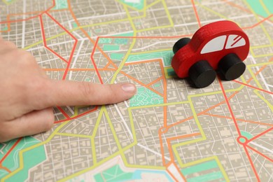 Photo of Woman pointing at city map near toy car, closeup. Road trip