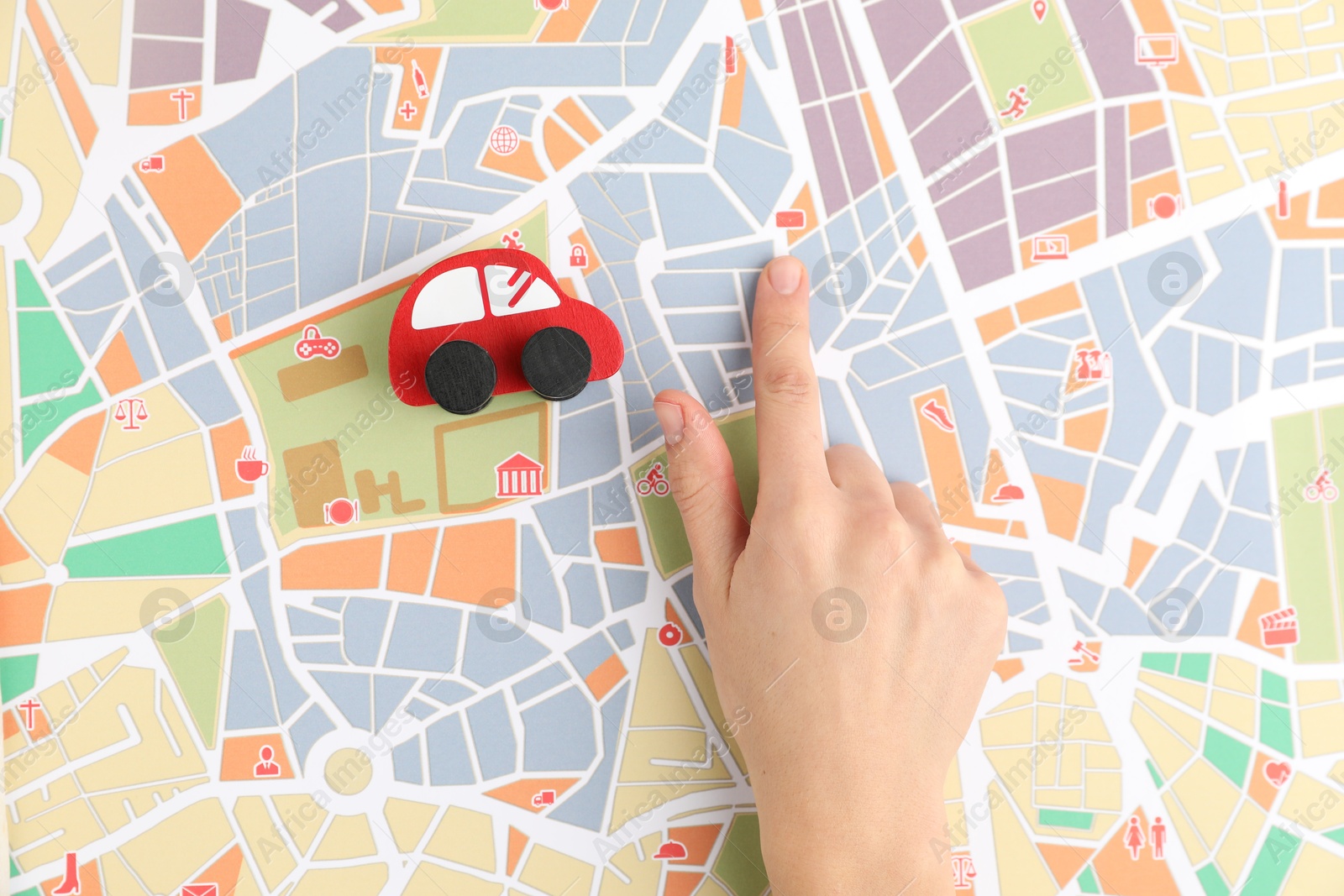 Photo of Woman pointing at city map near toy car, top view. Road trip