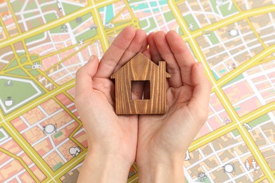 Photo of Woman with wooden house model near city map, top view. Accommodation search