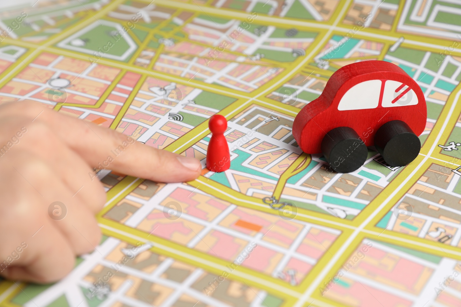 Photo of Woman pointing at city map with human figure and toy car, closeup. Road trip