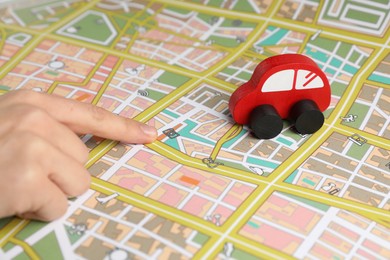 Photo of Woman pointing at city map near toy car, closeup. Road trip