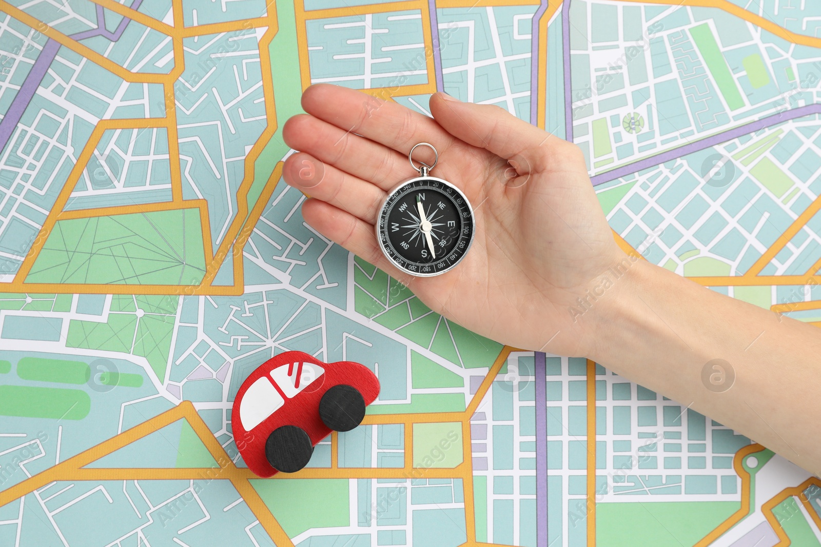 Photo of Woman holding compass near red toy car on city map, top view. Road trip