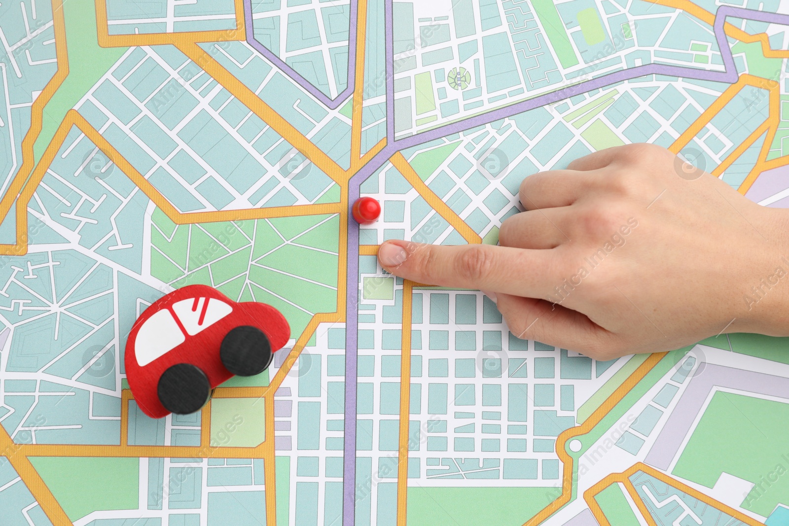 Photo of Woman pointing at city map near human figure and toy car, top view. Road trip