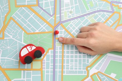 Photo of Woman pointing at city map near human figure and toy car, top view. Road trip