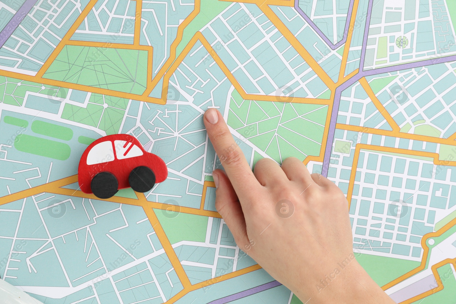 Photo of Woman pointing at city map near toy car, top view. Road trip