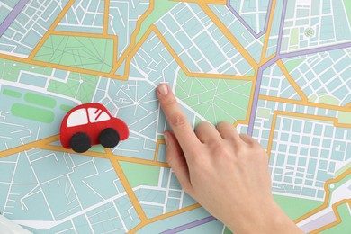 Photo of Woman pointing at city map near toy car, top view. Road trip