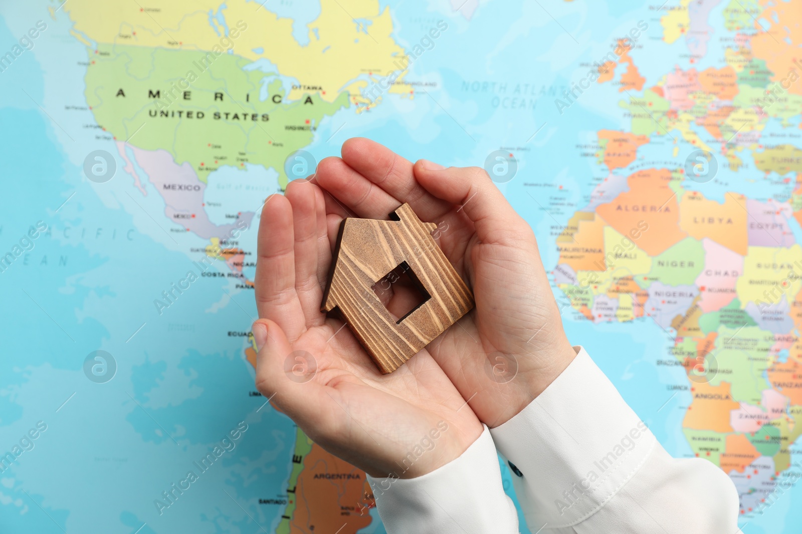 Photo of Woman holding wooden house model over world map, top view. Accommodation search