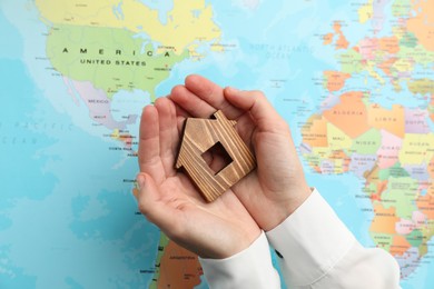 Photo of Woman holding wooden house model over world map, top view. Accommodation search