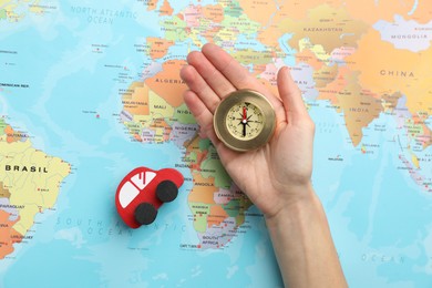 Photo of Woman holding compass near red toy car on world map, top view. Road trip