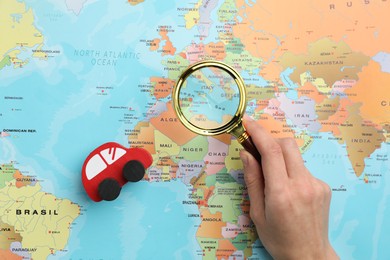 Woman looking at world map through magnifying glass, top view. Road trip