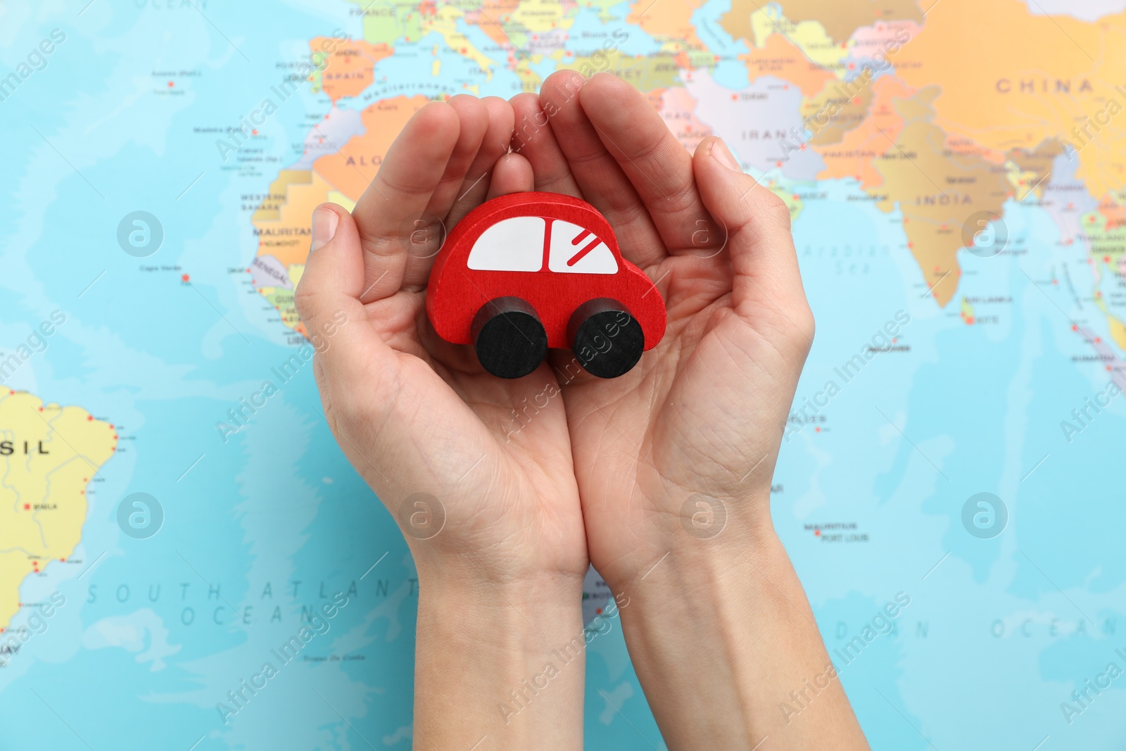 Photo of Woman holding red toy car over world map, top view