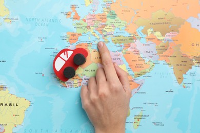 Photo of Woman pointing at world map near toy car, top view. Road trip