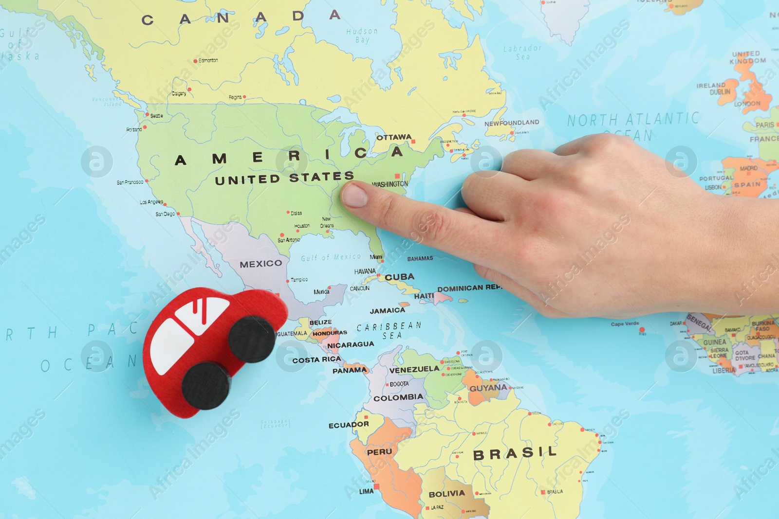 Photo of Woman pointing at world map with toy car, top view. Road trip