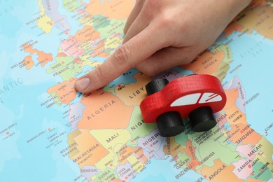 Photo of Woman pointing at world map with toy car, closeup. Road trip