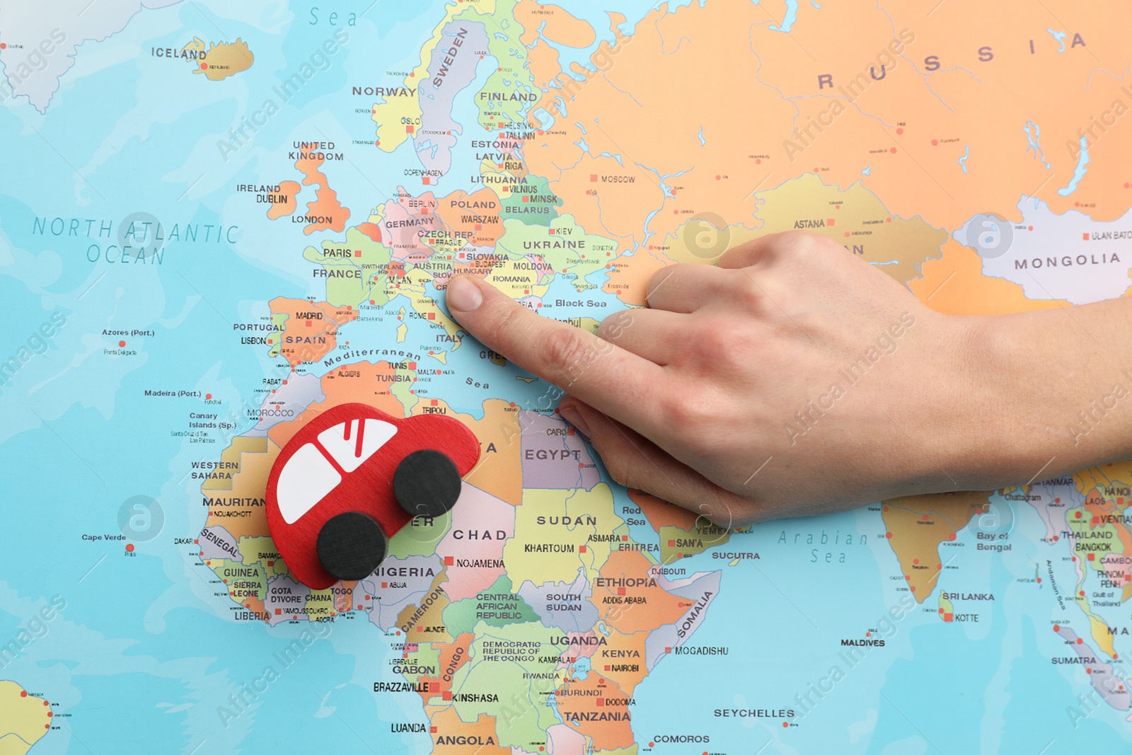 Photo of Woman pointing at world map with toy car, top view. Road trip